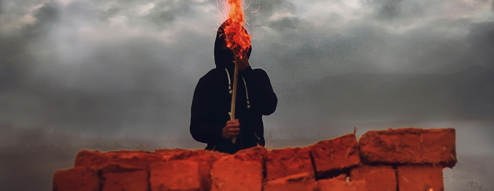 illustration-of-darkly-clothed-mystery-figure-holidng-a-flaming-torch-behind-bricks-to-illustrate-the-concept-of-a-human-firewall